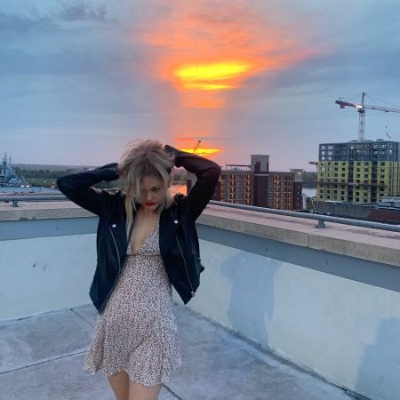 Emily Alyn Lind in a brown dress poses at the top of a building.
